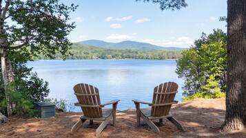 Dos sillas Adirondack mirando un lago con montañas al fondo.