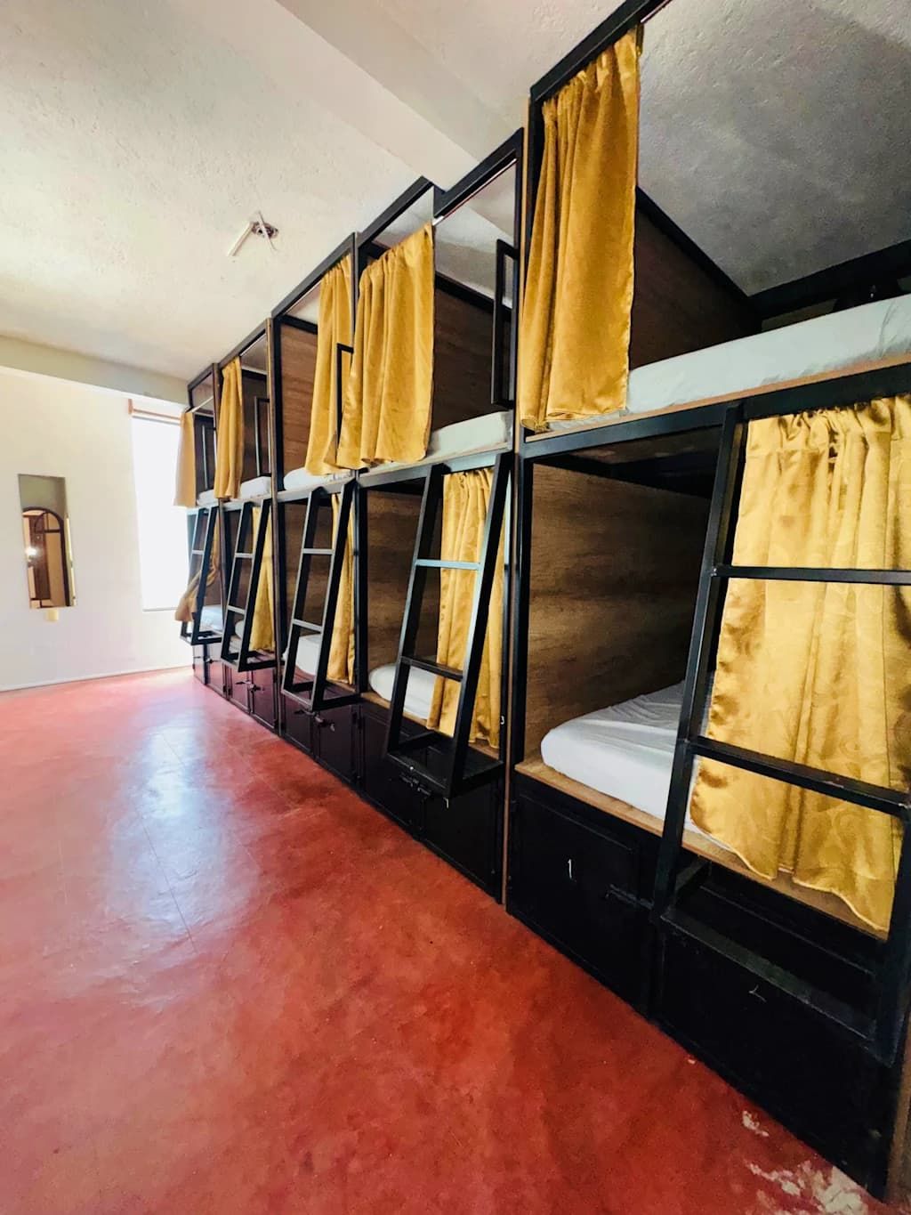 Varias literas con cortinas amarillas, piso rojo y pared blanca con una puerta.
