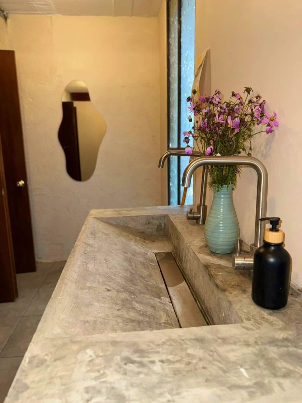 Un baño con lavamanos de mármol, un jarrón con flores y un dispensador de jabón.