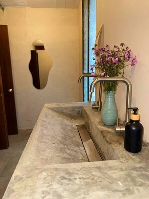 Un baño con lavamanos de mármol, un jarrón con flores y un dispensador de jabón.