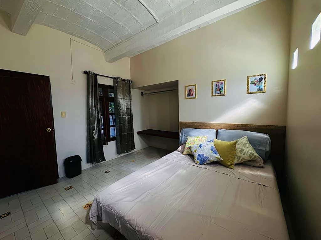 Quarto com cama, cabeceira de madeira, porta e janela com cortinas.