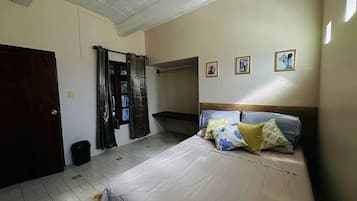 Quarto com cama, cabeceira de madeira, porta e janela com cortinas.