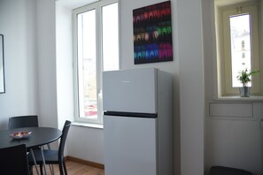 A kitchen with a white refrigerator, a dining table with chairs, and a window with a view of buildings. - Downtown Umberto 74 (Napoli)
