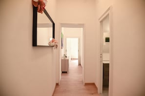 A hallway with a mirror, a door leading to a room, and a small table with a vase. - Downtown Umberto 74 (Napoli)
