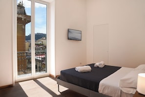 A hotel room with a bed, a TV, and a balcony with a city view. - Downtown Umberto 74 (Napoli)