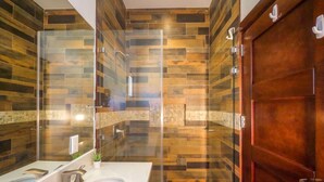 A modern bathroom with a glass-enclosed shower, a white sink with two faucets, and a wooden door. - Private Tropical Villa • Pool • Near Conchal & Flamingo (Brasilito)