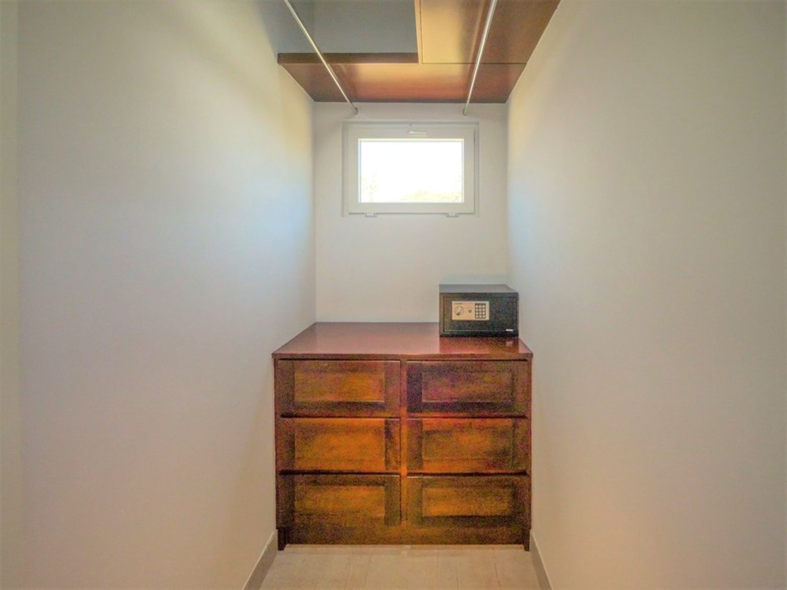 A small room with a wooden dresser, a window, and a ceiling light fixture.