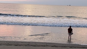 A beach scene with a person standing in the water, waves approaching the shore, and a distant landmass.