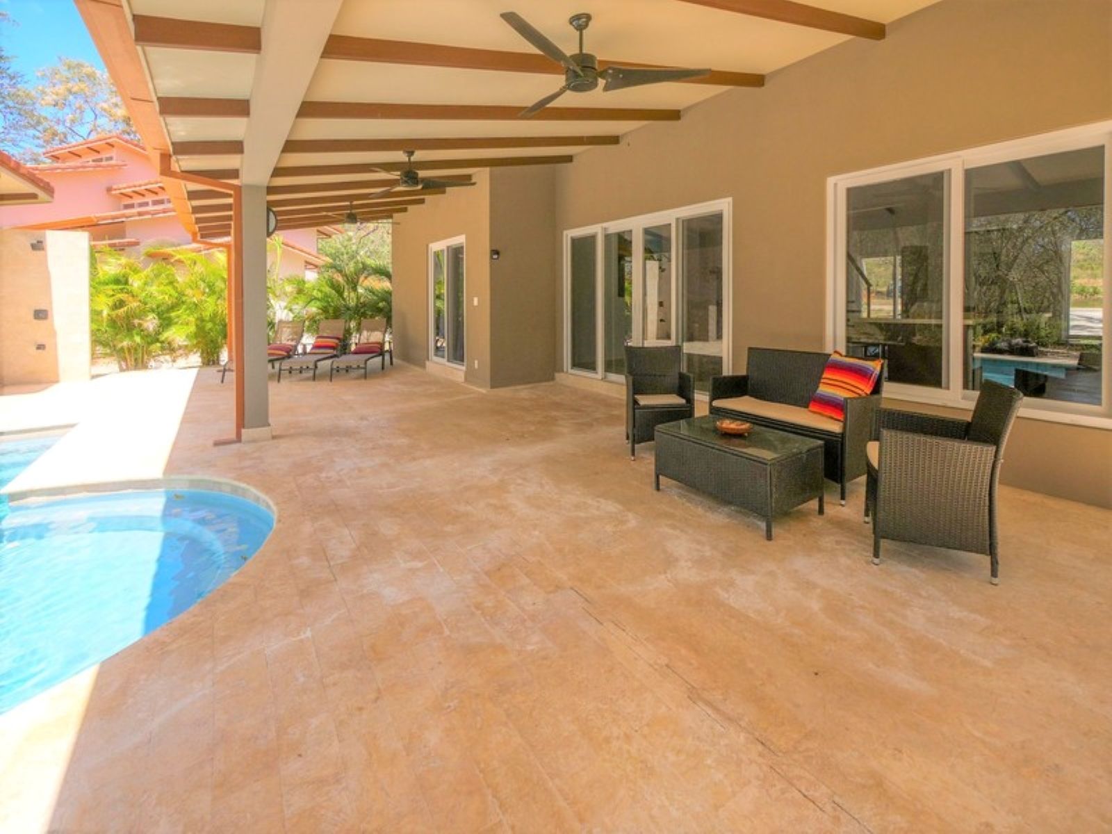 Área externa coberta com piscina, assentos e ventilador de teto.