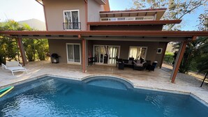 A swimming pool with a covered patio area, outdoor furniture, and a view of a building with multiple windows. - Private Tropical Villa • Pool • Near Conchal & Flamingo (Brasilito)