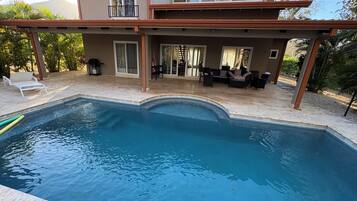 Une piscine avec un patio couvert, du mobilier d’extérieur et une vue sur un immeuble doté de nombreuses fenêtres.