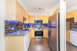 A modern kitchen with wooden cabinets, a stainless steel refrigerator, and a built-in oven. - Core Downtown condo with 2 bedroom 2  full bathrooms full equipment kitchen (Edmonton)