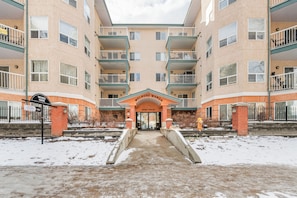 A multi-story building with a central entrance, balconies, and a snow-covered ground. - Core Downtown condo with 2 bedroom 2  full bathrooms full equipment kitchen (Edmonton)