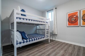 A bunk bed room with a window, wooden flooring, and two framed artworks on the wall. - Sleeps 24! 8 Bedrooms | Gameroom (Lake Hamilton)