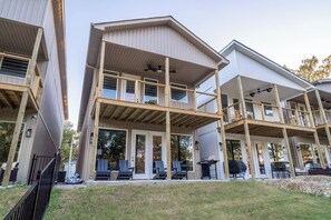 A multi-story building with a flat roof, large windows, and a covered outdoor seating area with chairs. - Sleeps 24! 8 Bedrooms | Gameroom (Lake Hamilton)