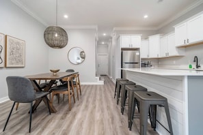 A modern kitchen with white cabinetry, a stainless steel refrigerator, and a dining area with a table and chairs. - Sleeps 24! 8 Bedrooms | Gameroom (Lake Hamilton)