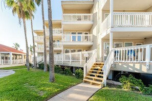 A multi-story residential building with balconies, a central staircase, and a small garden area with palm trees. - 6 Beds | Pool Steps Away | Private Beach Access (South Padre Island)