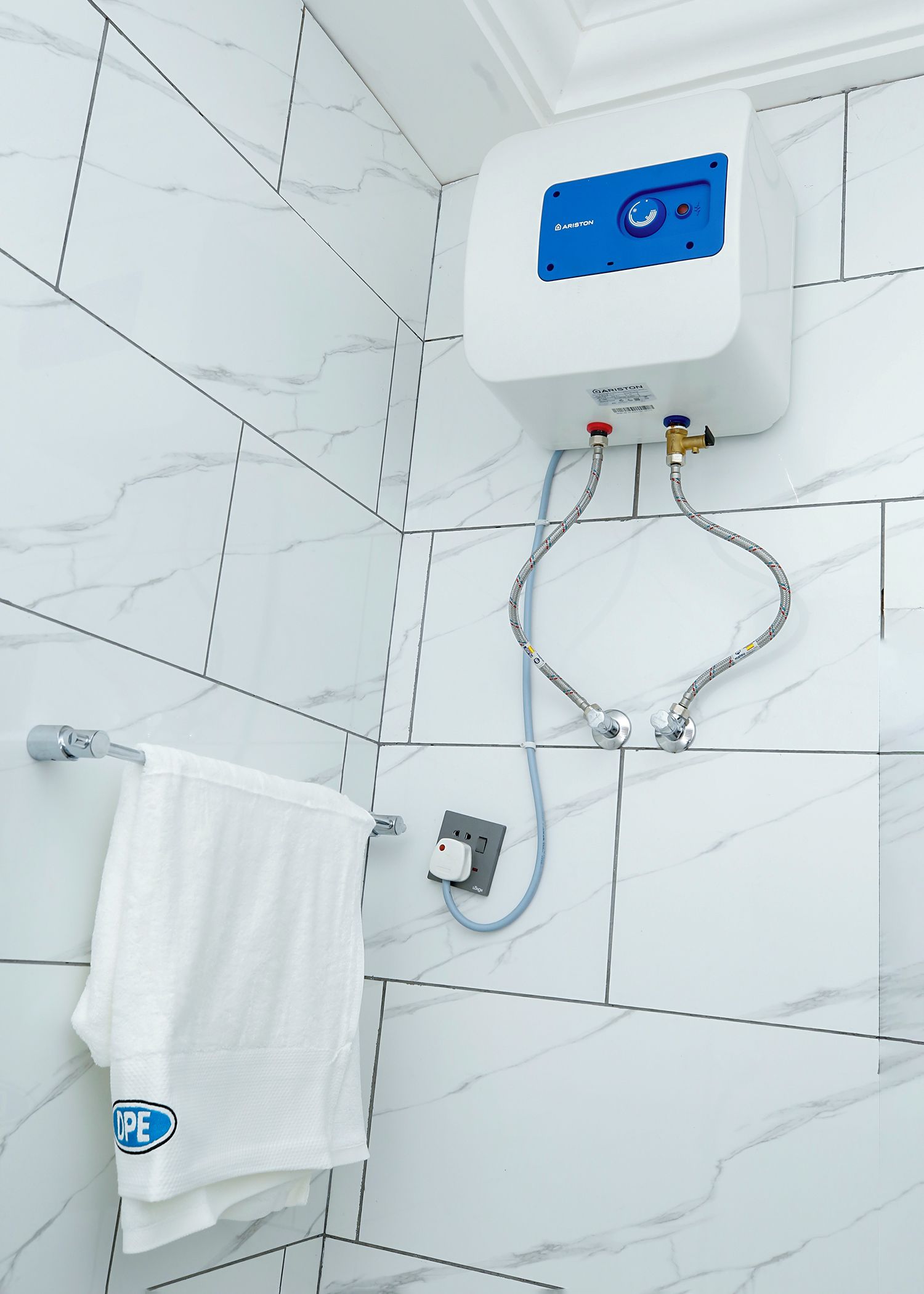 Een badkamer met witte marmeren tegels, een witte handdoek, een bedieningspaneel voor de douche aan de muur, en een handdouche.