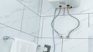 Een badkamer met witte marmeren tegels, een witte handdoek, een bedieningspaneel voor de douche aan de muur, en een handdouche.