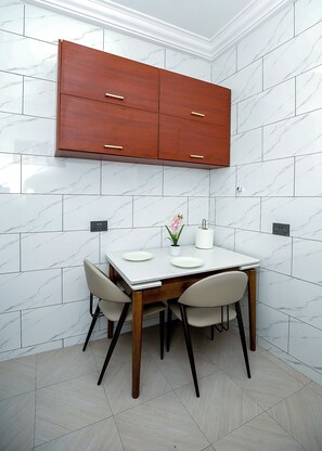 Una cucina moderna con piastrelle di marmo bianco, un armadietto in legno, un tavolo da pranzo con sedie e una piccola pianta in vaso.