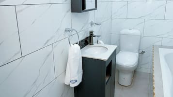Un bagno moderno con parete rivestita in marmo, mobile lavabo scuro, un water e un cestino.