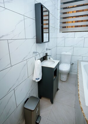 Un bagno moderno con parete rivestita in marmo, mobile lavabo scuro, un water e un cestino.