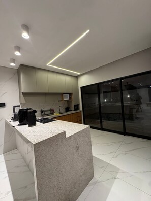 A modern kitchen with a central island, built-in appliances, and a large sliding glass door to the right. - Mangrove Refuge: A new, high-end home in the Brazilian Caribbean. (Barra Grande)