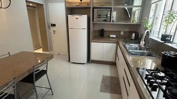 Cozinha moderna com geladeira, micro-ondas, fogão e área de refeições com mesa e cadeiras.