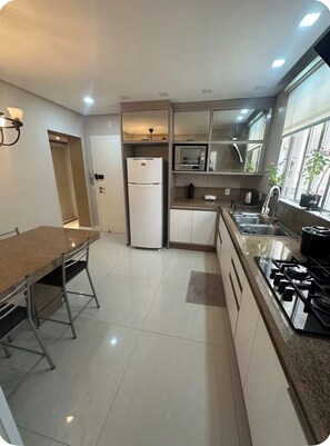 A modern kitchen with a refrigerator, microwave, stove, and a dining area with a table and chairs. - Luxo a 50m do Mar no centro de BC (Balneário Camboriú)