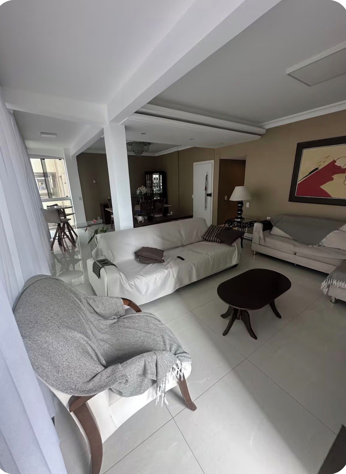Uma sala de estar ampla com sofá, poltrona, mesa de centro e uma área de jantar ao fundo.
