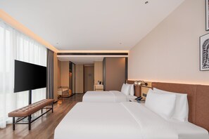 Une chambre d’hôtel dotée d’une grande télévision à écran plat, d’un banc, de deux lits, d’une table de chevet avec une lampe et d’un tableau encadré au mur.