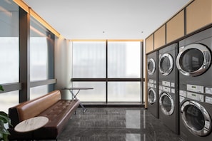 A laundry room with a bench, a table, and a row of washing machines. - Four Points By Sheraton Guangzhou Huangpu (Guangzhou)