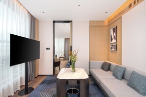 Una habitación de hotel moderna con una televisión de pantalla plana, un sofá, una mesita con un jarrón y un espejo que refleja la habitación.