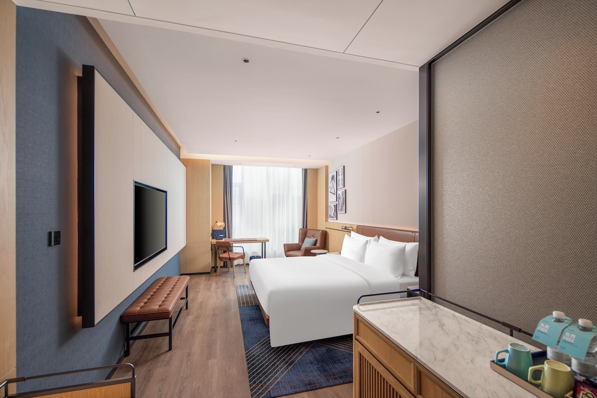 A hotel room with a bed, desk, chair, TV, and a large window.