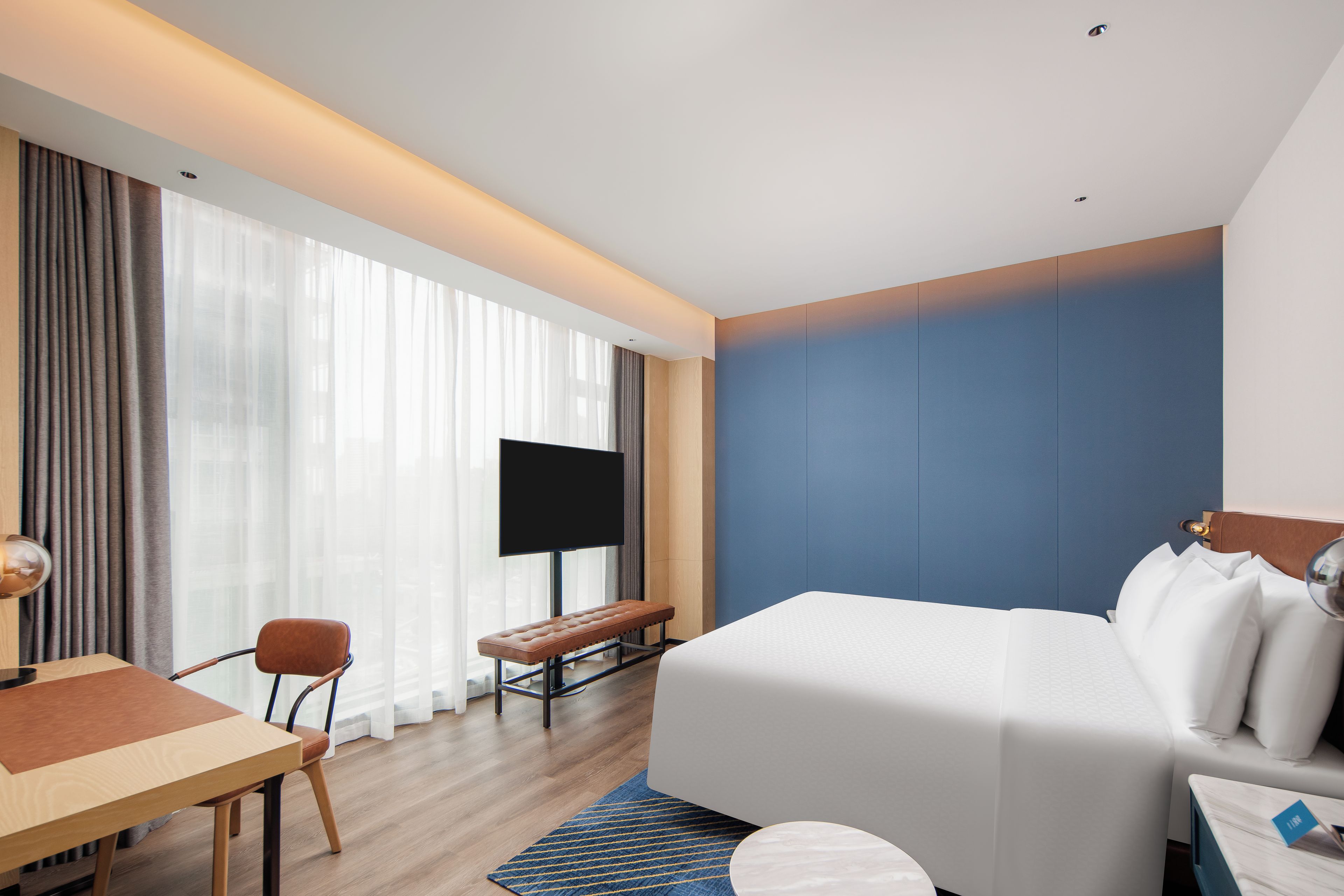 A hotel room with a bed, a desk, a chair, a television, and a window with curtains.