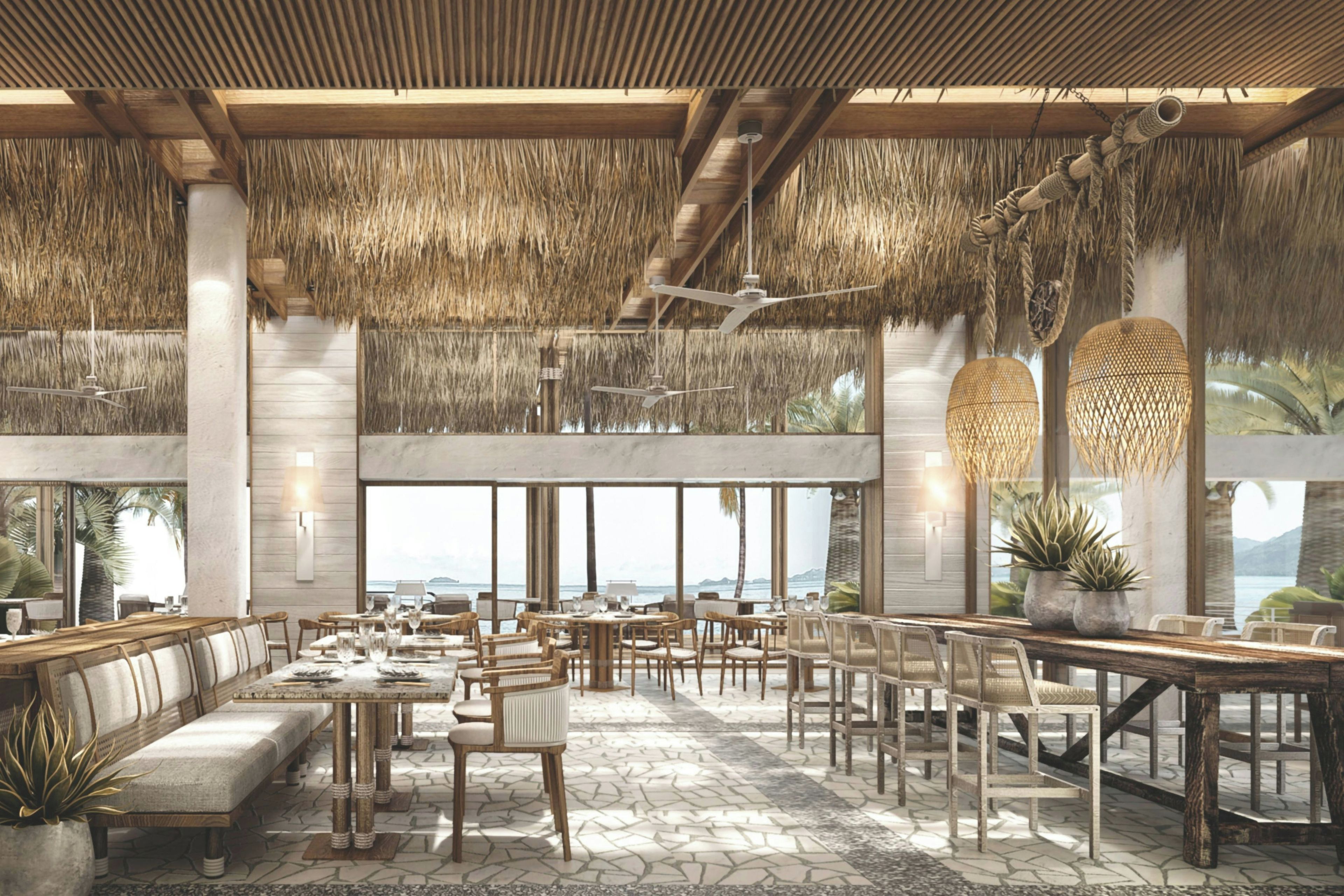 A spacious indoor area with high ceilings, thatched roof, and large windows offering a view of the sea.