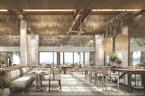 A spacious indoor area with high ceilings, thatched roof, and large windows offering a view of the sea.