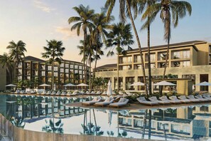 A resort with a swimming pool, lounge chairs, and palm trees.