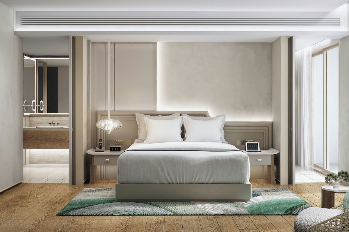 A modern bedroom with a large bed, bedside tables, a nightstand, a mirror, and a small potted plant.