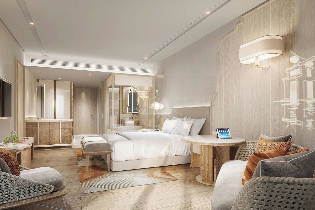 A modern hotel room with a large bed, bedside tables, a desk, and a seating area.