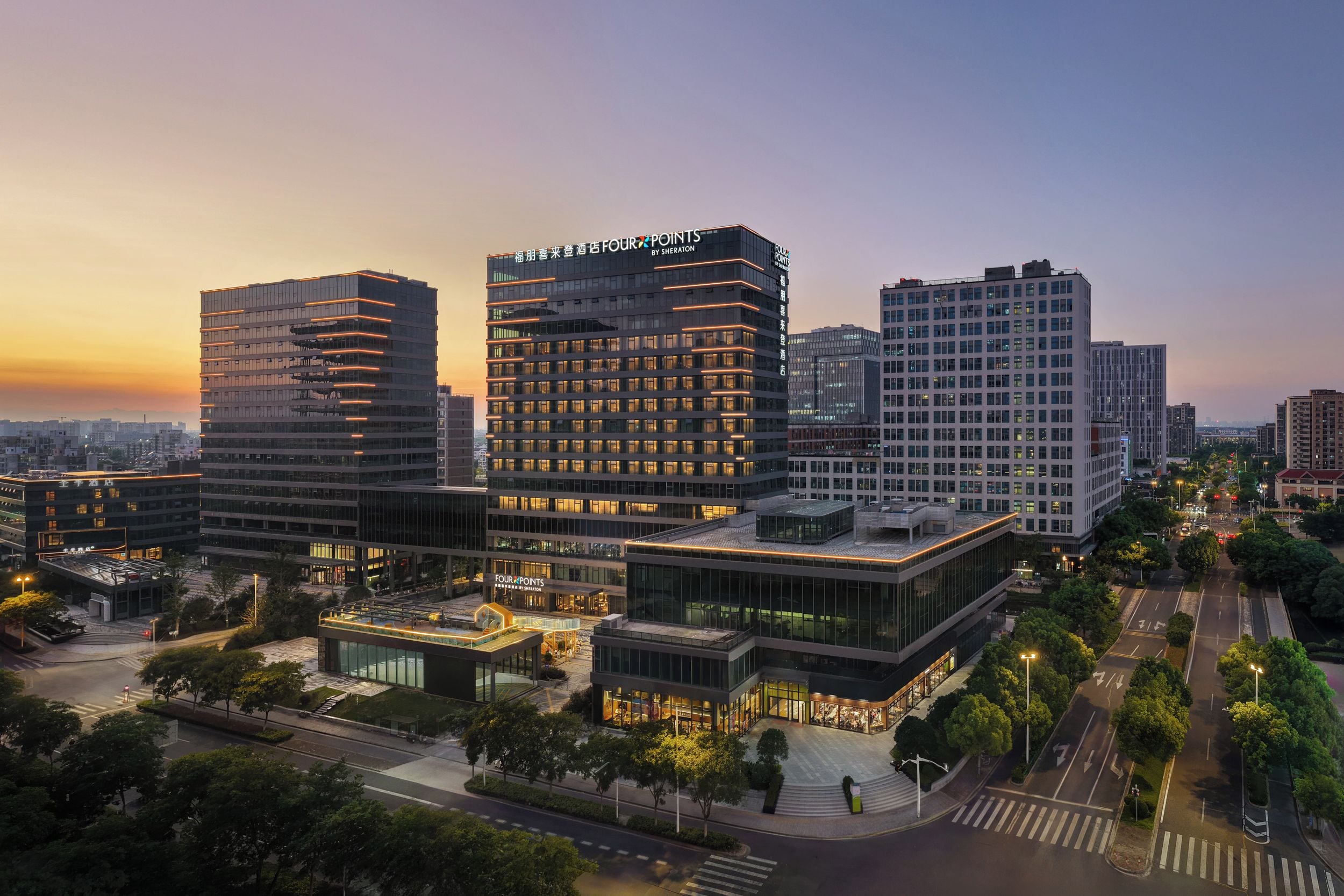 A modern hotel complex with multiple high-rise buildings, a well-lit entrance, and a clear sky.