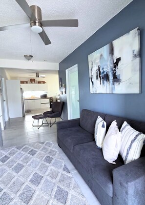 A modern living room with a gray sofa, a ceiling fan, and abstract wall art. - Azulena - A stay between the mountains & sea! With Tesla battery & water tank (Fajardo)