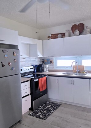 A modern kitchen with white cabinets, stainless steel appliances, a black oven, and a window above the sink. - Azulena - A stay between the mountains & sea! With Tesla battery & water tank (Fajardo)