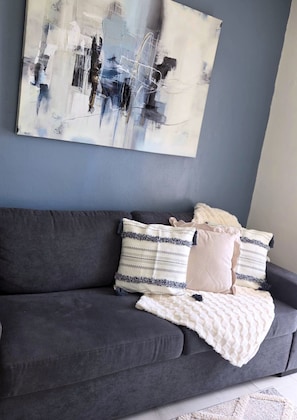 Un sofá gris con cojines estampados y una manta blanca.