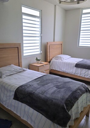 Ein Schlafzimmer mit zwei Betten, einem Nachttisch mit Pflanze und einem Fenster mit Jalousien.