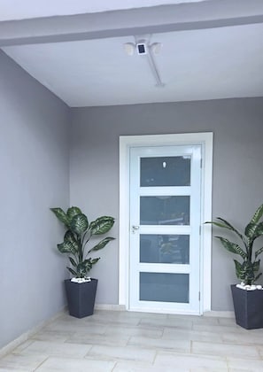 A door with a white frame and glass panels, flanked by two potted plants with broad leaves. - Azulena - A stay between the mountains & sea! With Tesla battery & water tank (Fajardo)