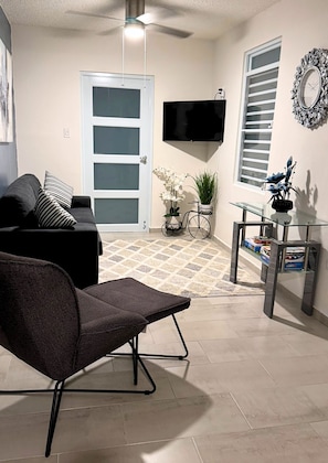 Ein Wohnzimmer mit einer Couch, einem Sessel, einem Fernseher, einem Fahrrad und einem kleinen Tisch mit Büchern.