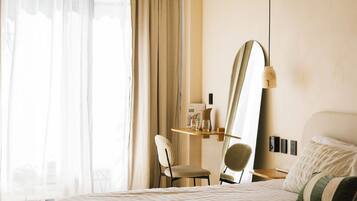 Una habitación de hotel con una cama, una silla, un escritorio con lámpara, un espejo y una ventana con cortinas.