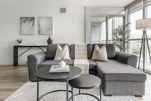 A modern living room with a grey sectional sofa, a round coffee table, and a black console table with decorative items. - Spacious Downtown 2BR plus Den Free Parking & Patio! | Parking Available (Toronto)