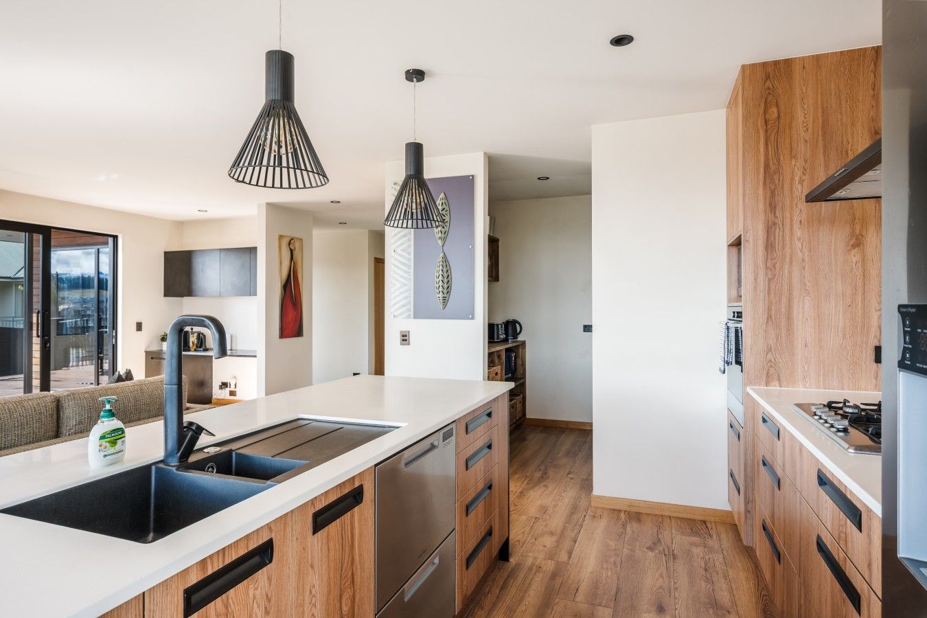 A modern kitchen with a central island, wooden cabinets, stainless steel appliances, pendant lighting, and a view to the outside.